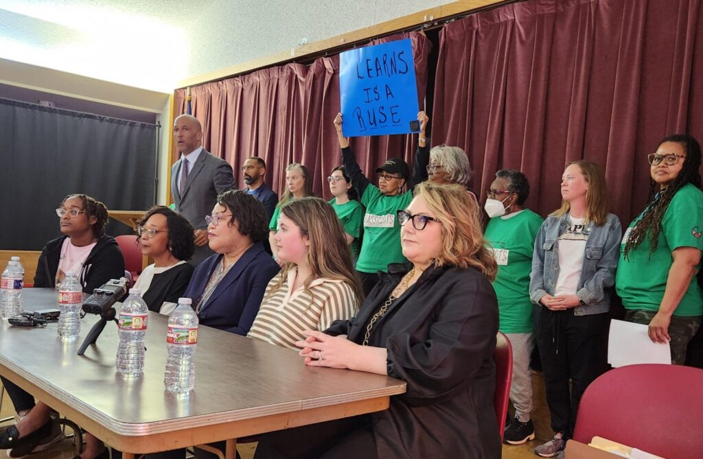 From left front: Gisele Davis, Chandra Williams-Davis, Ruthie Walls, Sadie Belle Reynolds and Jennifer Reynolds are five of the seven plaintiffs challenging Section 16 of the Arkansas LEARNS Act in federal court. Mike Laux (at podium) is one of their attorneys and filed the lawsuit Monday, March 25, 2024 before hosting a news conference at Bullock Temple CME Church, across the street from Little Rock Central High, where Gisele and Sadie Belle are students in Walls’ AP African American Studies course. (Tess Vrbin/Arkansas Advocate)